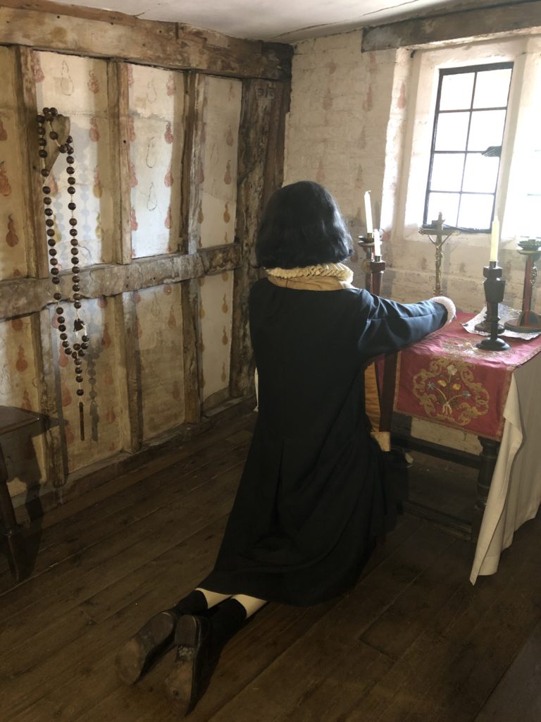 Figure of a priest in Elizabeth dress kneels in front of a Catholic altar