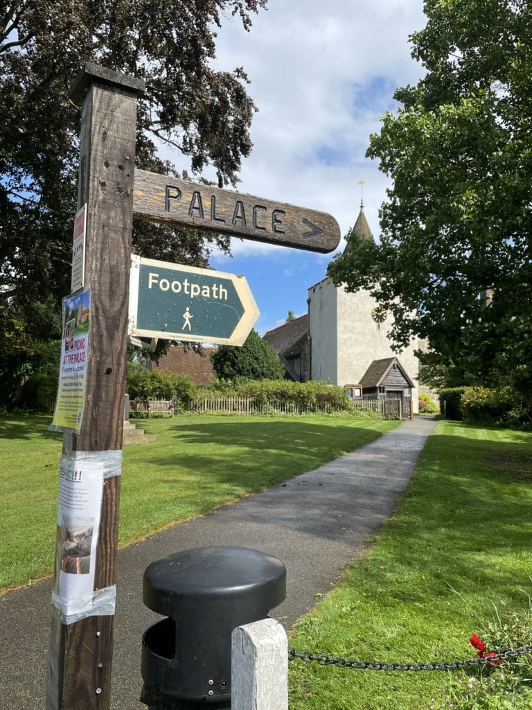 A wooden signpost with the words 'palace' written on it and a church in the background