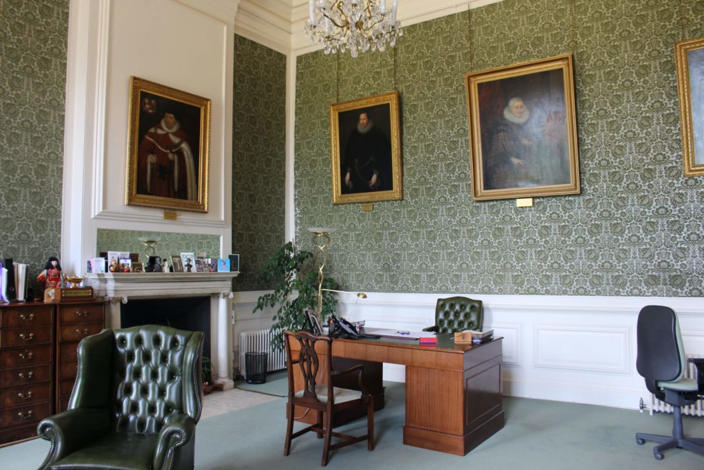 A room where Katherine of Aragon died at Kimbolton castle with chairs, a desk and portraits on the wall.