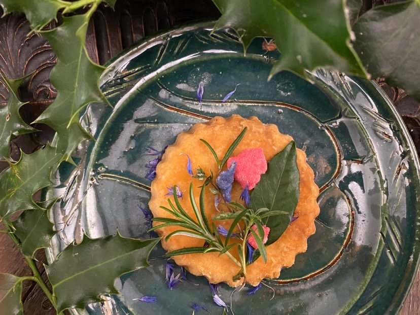 A venison pie on a green plate and decorated by herbs and edible flowers.