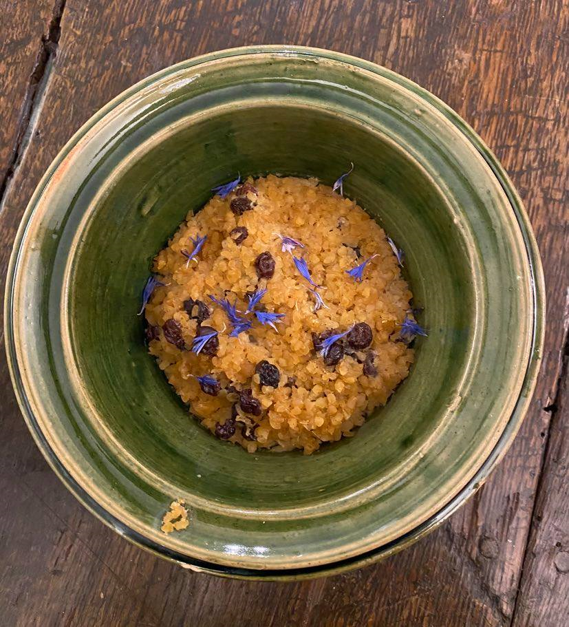 A bowl of Tudor food, baked wheat and currents decorated with small purple flowers