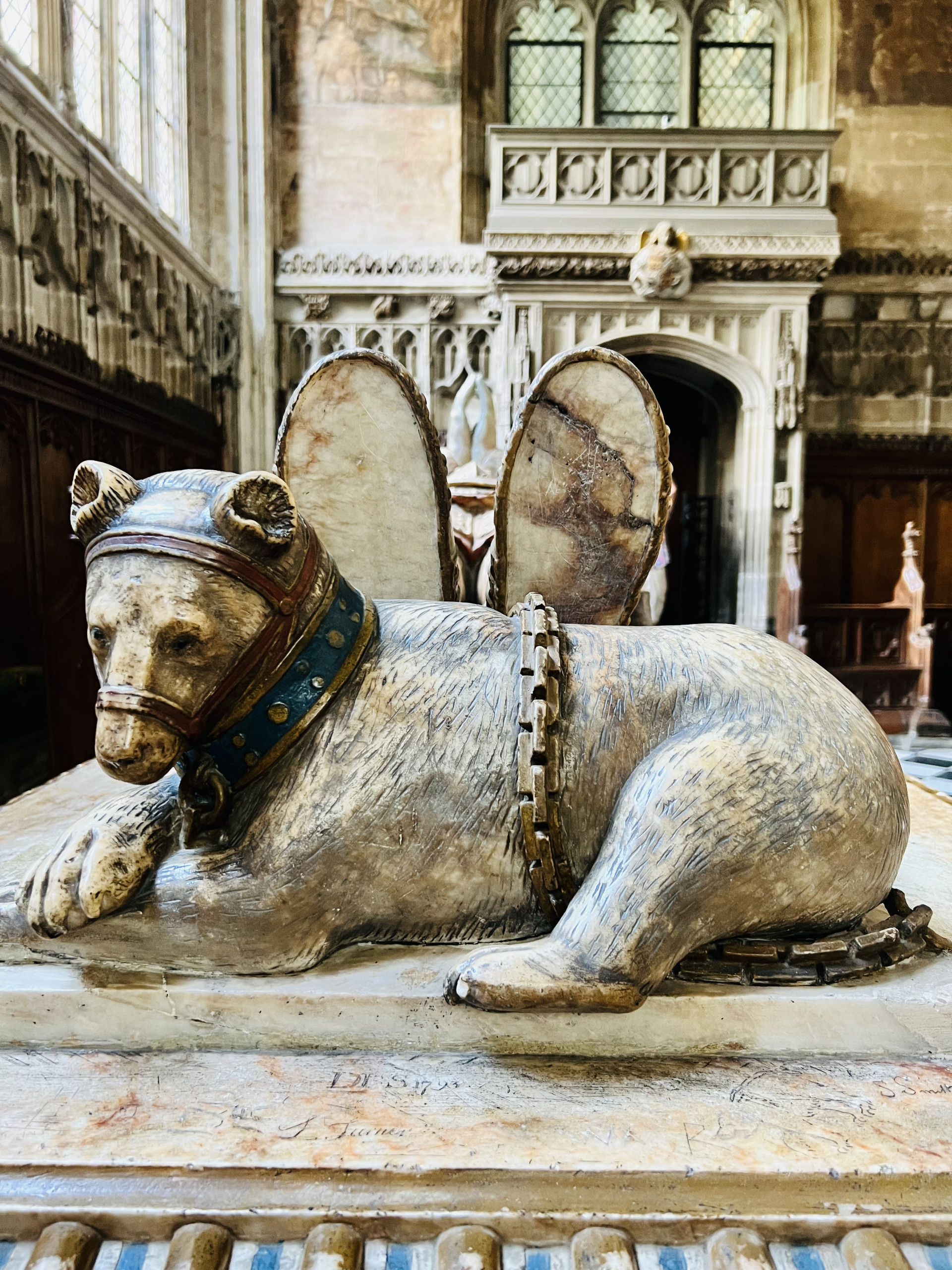 A bear lying in chains at the feet of a tomb effigy.